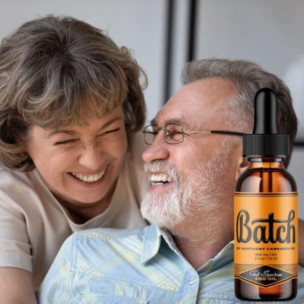Front view of Batch CBD Oil 2 oz bottle by Kentucky Cannabis Company, alongside a happy husband and wife. The bottle contains 900 mg of full spectrum CBD extract.