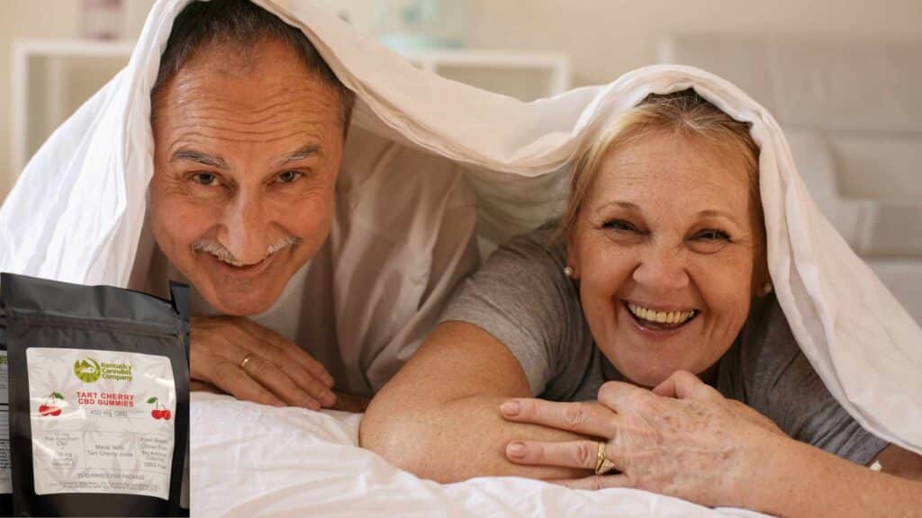 A man and woman playfully relaxing in bed, smiling with their heads popping out of the sheets, suggesting the relaxing effects of CBD gummies for wellness and intimacy.